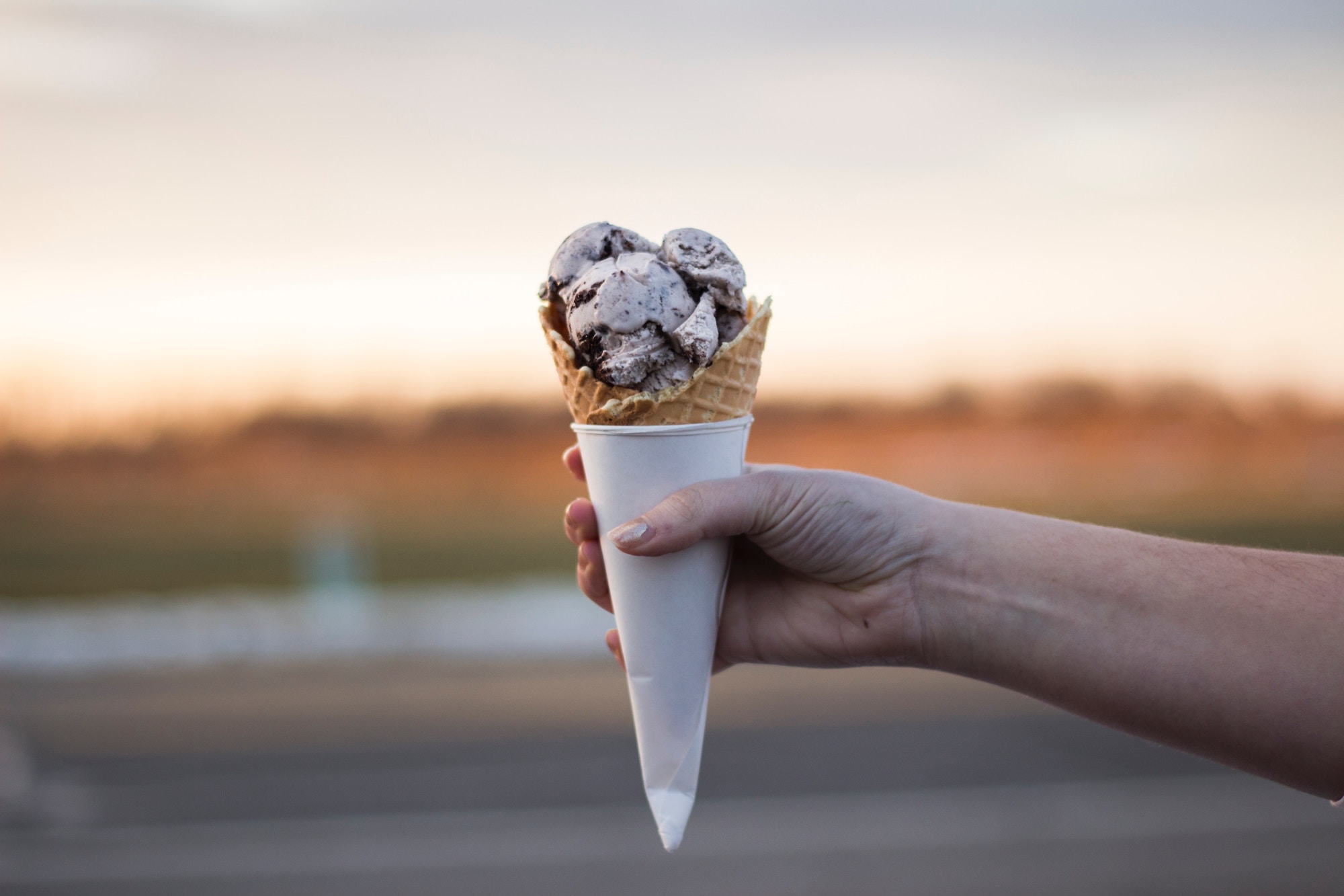 Frau hält eine Waffel mit 3 Kugeln Eis in der Luft